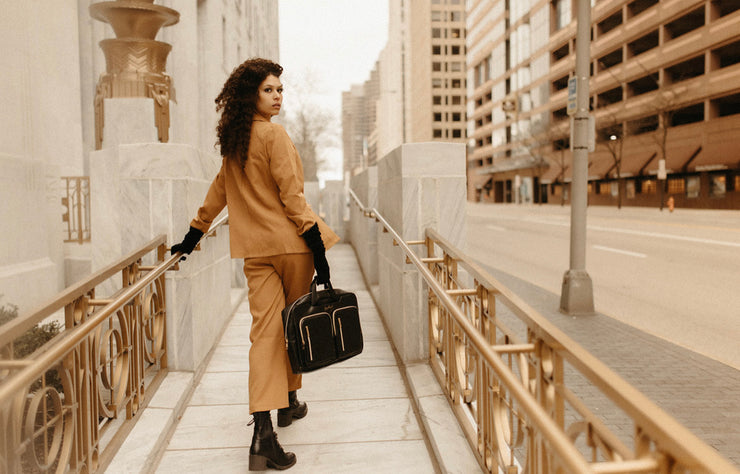 Stylish woman with briefcase Professional woman in city Fashionable business attire Urban street style with briefcase Young professional navigating city Elegant tan suit and briefcase Cityscape background with professional woman Woman with black leather briefcase
